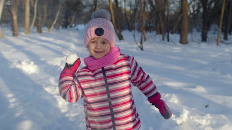 Child-girl-throwing-snowball-into-camera,-smiling-kid-walking,-playing-with-snow-in-winter-park