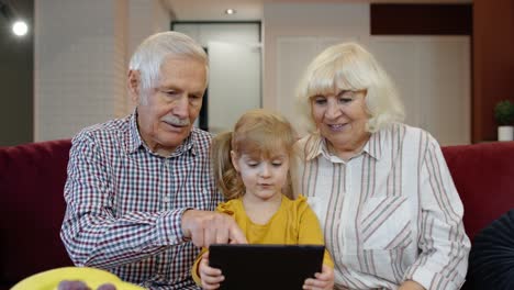 Child-girl-shows-something-in-laptop-to-grandparents,-seniors-couple-learning-how-to-use-tablet