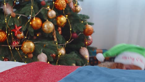 Toddler-girl-in-Santa-Claus-Elf-pajama-hiding-behind-bed,-playing-hide-and-seek-game,-Christmas-tree