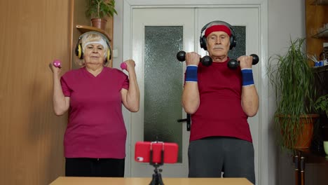 Senior-elderly-couple-watching-online-workout-exercises-on-mobile-phone-and-training-with-dumbbells