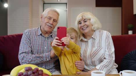 Senior-couple-grandparents-with-child-granddaughter-making-selfie-photos-together-on-mobile-phone