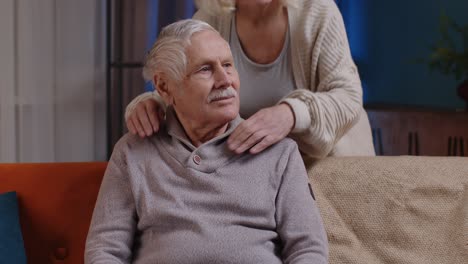 Happy-old-senior-elderly-family-couple-hugging,-smiling,-smiling-looking-at-camera-at-home-sofa