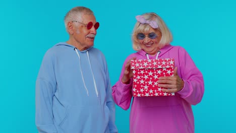 Cheerful-senior-couple-man-woman-grandparents-opening-gift-box,-smiling-joyfully-birthday-surprise