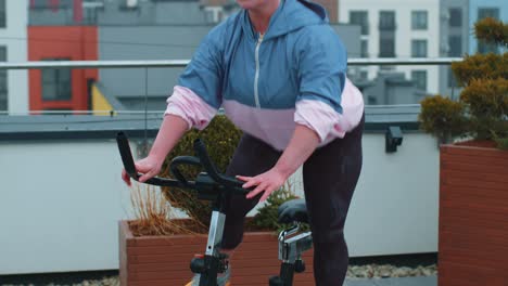 Sportliche-Frau-Reitet-Auf-Einem-Stationären-Fahrrad-Und-Trainiert-Auf-Dem-Hausdach,-Gewichtsverlust
