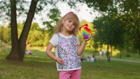 Child-girl-holding-many-colorful-squishy-silicone-bubbles-pop-it-popular-sensory-toys,-thumb-up