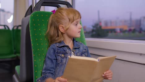 Portrait-of-attractive-little-child-girl-kid-sitting-at-empty-subway-train,-reading-interesting-book