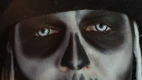 Close-up-shot-of-face-in-skeleton-Halloween-makeup-opening-eyes-with-white-pupil,-trying-to-scare