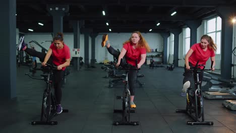 Group-of-smiling-friends-women-class-exercising,-training,-spinning-on-stationary-bike-at-modern-gym
