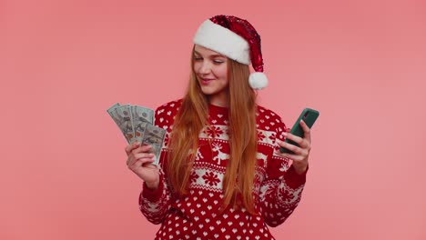 Frau-Im-Weihnachtspullover-Schaut-Aufs-Smartphone-Und-Freut-Sich-Aufrichtig-über-Erfolg-Und-Glück-Beim-Geldverdienen