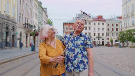 Älterer-Alter-Tourist,-Mann-Und-Frau-Gehen-Mit-Smartphone-Auf-Selfie-Stick-Durch-Die-Stadt-Und-Machen-Fotos