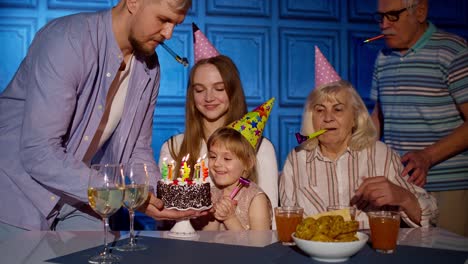 Girl-celebrating-birthday-party-with-parents,-senior-grandparents-family-blowing-out-candles-on-cake