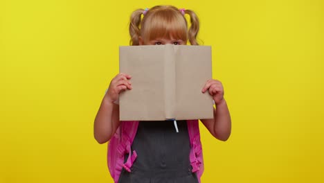 Funny-kid-primary-school-girl-with-ponytails-wearing-uniform-peeping-while-hiding-behind-a-book