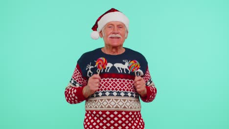 Senior-grandfather-in-Christmas-sweater-holding-candy-striped-lollipops,-dancing-making-silly-faces