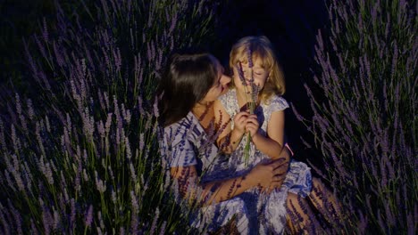 Mother-and-girl-daughter-kid-kissing,-laughing-in-aromatic-flowers-lavender-field-garden-at-night