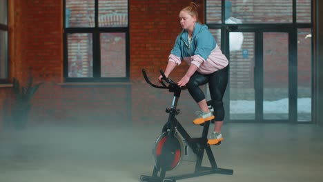Healthy-Caucasian-woman-exercising-workout-on-stationary-cycling-machine-bike-in-gym,-slow-motion