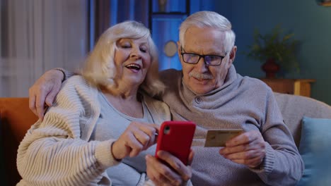Ältere-Großmutter,-Großvater-Mit-Mobiltelefon-Zu-Hause,-Die-Online-Einkäufe-Mit-Kreditkarte-Macht