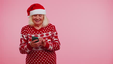 Grandmother-Santa-Christmas-sweater-with-mobile-phone-showing-pointing-empty-place,-advertising-area