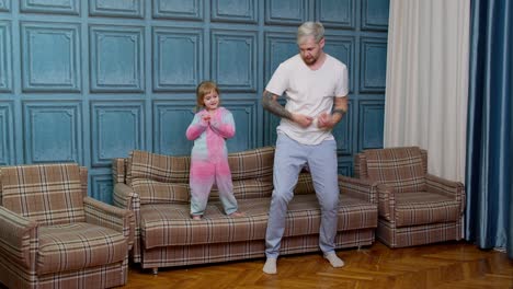 Happy-funny-family-father-and-child-kid-daughter-dancing,-jumping-on-sofa,-listening-music-at-home