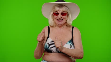 Elderly-woman-tourist-in-swimsuit-and-sunglasses,-looking-at-camera,-smiling,-showing-thumbs-up