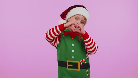 Smiling-girl-in-Christmas-Elf-costume-makes-heart-gesture-demonstrates-love-sign-expresses-feelings
