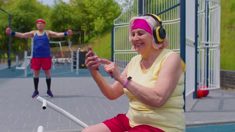Senior-woman-after-sport-training-listening-music-from-mobile-phone-wearing-headphones-on-playground