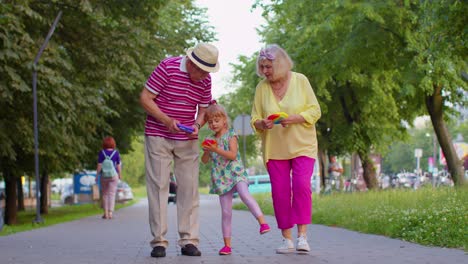 Senior-grandmother-grandfather-walking-with-granddaughter-and-playing-anti-stress-pop-it-toy-game