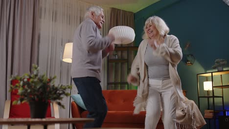 Glückliches-älteres-Paar-Tanzt-Zu-Hause-Entspannt-Und-Hat-Spaß-Mit-Moderner-Musik,-Die-Zu-Hause-Lächelt