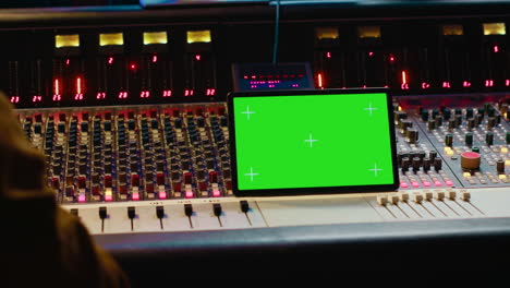 Music-producer-holding-a-tablet-with-greenscreen-display-on-mixing-console