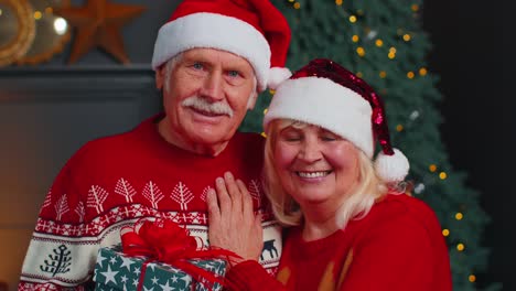 Mature-couple-family-in-Santa-Claus-hats-celebrating-Christmas-looking-at-camera-and-hugging-at-home