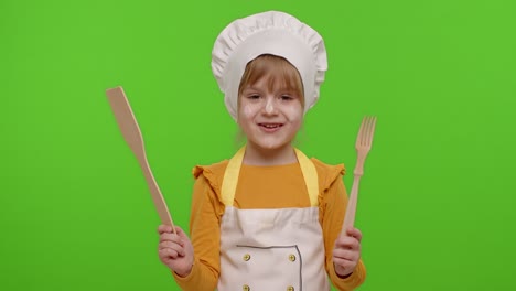 Child-girl-kid-dressed-as-cook-chef-showing-wooden-fork-and-spatula,-smiling,-dancing-on-chroma-key