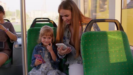 Child-girl-with-mother-using-mobile-phone-internet-social-network-application-while-traveling-by-bus