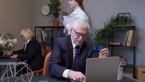 Senior-businessman-grandfather-director-shopping-online-and-paying-with-credit-card-in-modern-office
