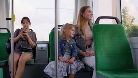 Family-rides-in-public-transport,-woman-with-little-child-girl-sit-together-and-look-out-window-tram