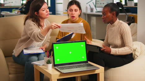 Diverse-women-sitting-at-table-discussing-strategy-with-green-screen-laptop