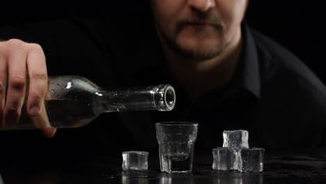 Bartender-man-pouring-up-frozen-vodka,-sake-from-bottle-into-shot-glass-with-ice-cubes-and-drinking