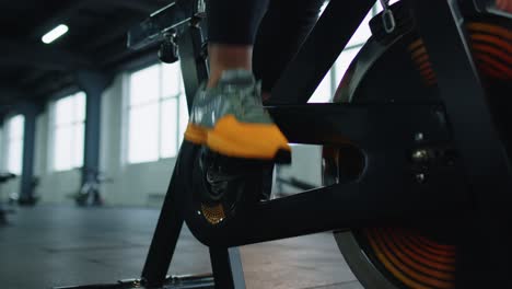 Close-up-athletic-woman-leg-spinning-exercising-workout-on-stationary-cycling-machine-bike,-indoors