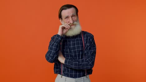 Senior-smiling-old-man-with-gray-haired-looking-at-camera,-fixing-beard-posing-on-orange-background