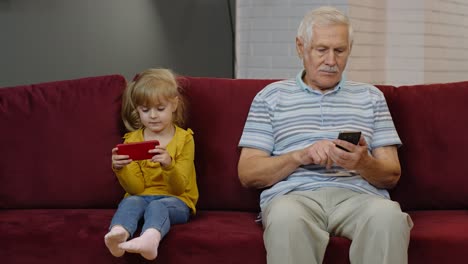 Senior-grandfather-with-child-girl-granddaughter-using-digital-mobile-phone,-playing-games-at-home