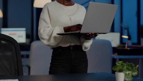 African-freelancer-looking-at-camera-smiling-holding-laptop-standing-near-desk