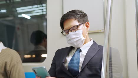 Reisender-Trägt-Gesichtsmaske,-Während-Er-Im-öffentlichen-Zug-Sein-Mobiltelefon-Benutzt