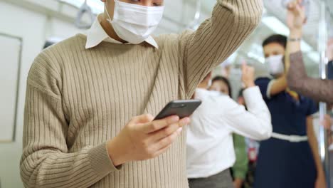 Traveler-wearing-face-mask-while-using-mobile-phone-on-public-train