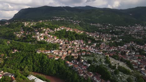 Aerial-drone-view-of-the-city-built-on-the-green-mountainside,-cloudy-sky