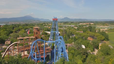 Winding-and-twisting-blue-tracks-of-large-roller-coaster-tower-over-amusement-park-by-Lake-Garda-Italy