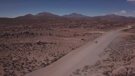 Aerial-view-of-a-4x4-on-a-dusty-red-road-at-the-Eduardo-Avaroa-National-Andean-Wildlife-Reserve,-slowly-lifting-the-view-to-open-up-to-the-valley-of-rocks,-"Valle-de-Rocas"-in-Uyuni,-Bolivia