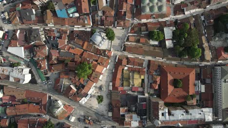 Drone-view-from-above-of-roofed-houses-and-mosques-of-Bosnian-city,-vehicles-pass-through-the-streets-and-avenues