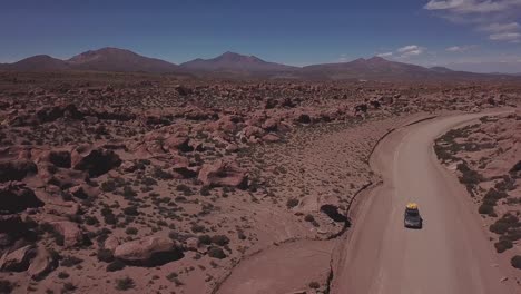 Vista-Aérea-De-Un-4x4-En-Un-Polvoriento-Camino-Rojo-En-La-Reserva-Nacional-De-Vida-Silvestre-Andina-Eduardo-Avaroa,-Levantando-Lentamente-La-Vista-Para-Abrirse-Al-Valle-De-Rocas,-&quot;valle-De-Rocas&quot;-En-Uyuni,-Bolivia