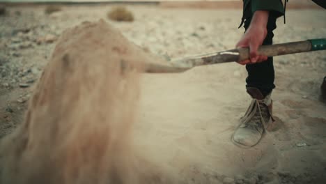 Man-shovels-dusty-sandy-soil-in-desert-with-spade,-low-angle-slow-motion