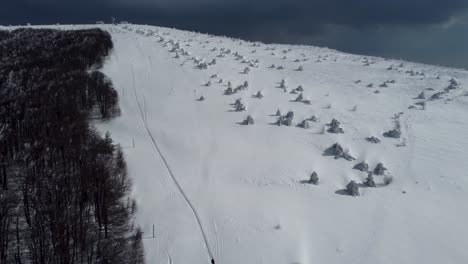 Aerial-pan-of-snowy-forest-and-mountaineers-near-Chumerna-peak,-Bulgaria