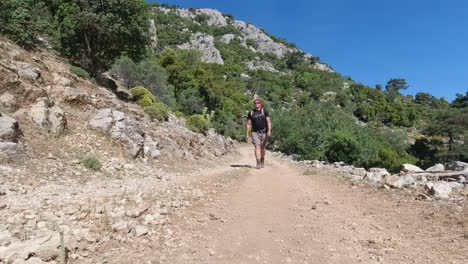 Man-with-backpack-hiking-on-rocky-mountain-on-dirt-road-on-Lycian-Way,-Turkey