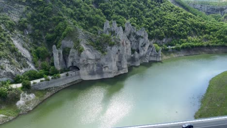 Road-passes-under-iconic-rock-formations-next-to-Tsonevo-reservoir,-aerial